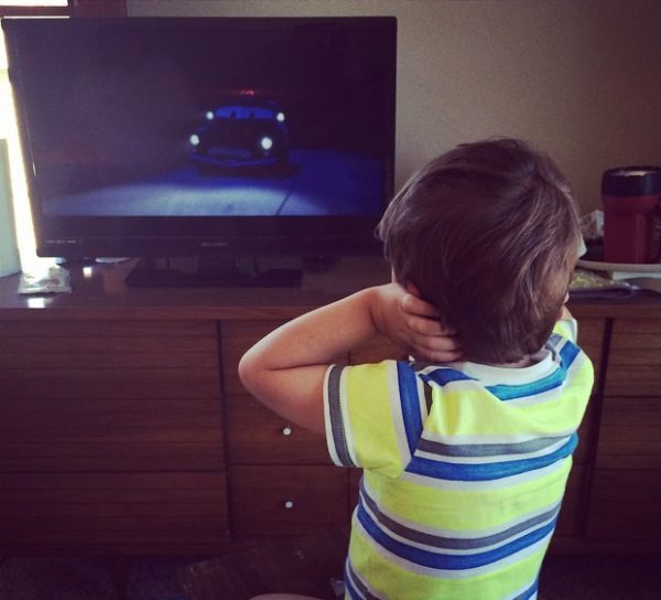 Photo is shows a child covering their ears while watching tv