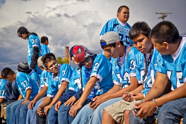 Photo of ten boys sitting together all wearing matching blue football jerseys. Some have blue face paint under their eyes. 