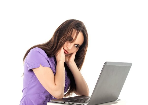 A stressed-out woman holds her head and looks at her computer.